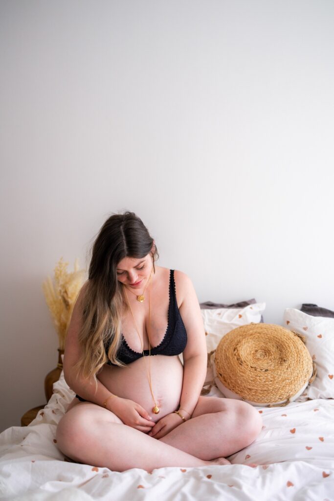 Femme enceinte assise en tailleur sur le lit, mains sur le ventre