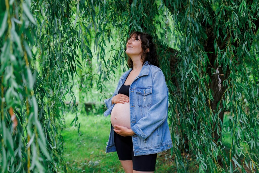 Future maman sous un saule pleureur, regard vers le ciel, ventre dévoilé, séance en pleine nature — photographe grossesse Cergy