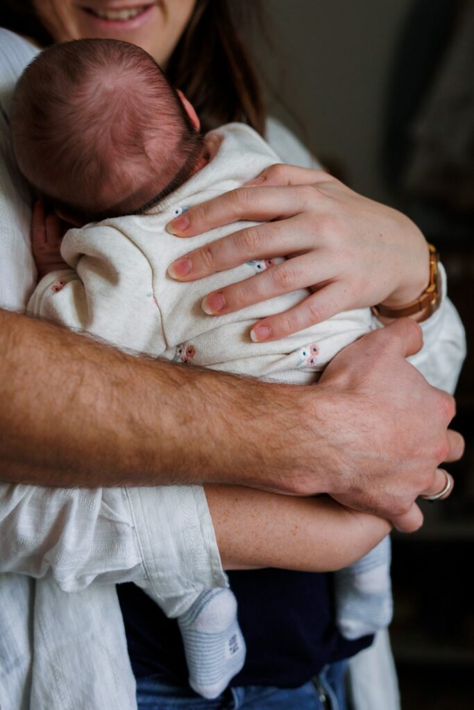 Gros plan sur les mains des parents enlaçant la tête du bébé, tenue à motifs fleuris